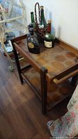 Wooden teacart with upper and lower shelves, visible stains, placed near wall, several collectible bottles on top