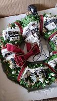 Full view of the wreath showing the miniature snow-covered village houses, green foliage, and attached electric cord for lighting.