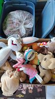 Box shows a variety of plush toys including TY Babies, Taco Bell dogs, Looney Tunes Bugs Bunny and Energizer Bunny plush toys, stuffed in a cardboard box needing cleaning.