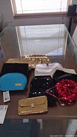 Nine vintage women's purses and one blue makeup bag on a glass table showing variety of colors and styles.