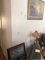 View of corner with some framed prints leaning against wall and a large lighthouse print hanging above couch
