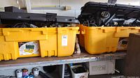Two large yellow totes with black lids filled with water softener parts on a shelf, showing quantity and container condition.