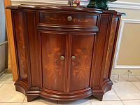 Front view of wood cabinet with floral inlay on drawer and doors, showing brass knobs and curved molding details.