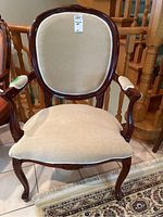 Front view of wooden arm chair showing beige cushioned seat and backrest, with carved wood frame and armrests.