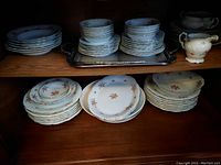 Full view of dinnerware set on shelves including stacked plates, bowls, creamer, sugar bowl, and metal trays showing floral pattern and arrangement