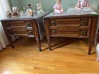 Two matching wood end tables with carved details and covered with bubble wrap on top. Various figurines visible on top but not included.