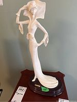 Full body view of the A. Santini figurine of a lady wearing a large flowing hat and elegant dress, standing on a dark wooden base showing full height and form.