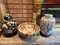 View of two lidded ceramic jars on stands and ceramic bowl on a stone surface in front of a fireplace