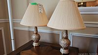 Pair of vintage ceramic table lamps with pleated beige fabric shades on a wooden surface against a neutral wall.