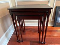 Set of three nested dark wood tables showing varying heights and tapered legs with rounded feet.