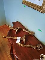 Two gold-tone Hennessy wall sconces resting on a wooden furniture piece, showing full length and design.