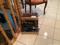 Singer electric portable sewing machine placed inside original brown carrying case with gold trim, visible power cord.