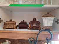 Four ornate decorative trinket boxes arranged on a shelf showing variety in shape, material, and decoration
