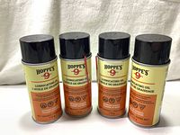 Four cylindrical cans of Hoppe's No. 9 Lubricating Oil with black caps, arranged in a row against a white fabric background.