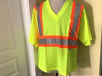 Front view of brand new neon yellow mesh safety T-shirt with short sleeves, V-neck, 3M Scotchlite reflective gray and orange stripes, and left chest pocket.