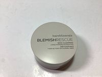 Top view of closed beige container with 'bareMinerals BLEMISH RESCUE SKIN-CLEARING LOOSE POWDER FOUNDATION DETOXIFICATION' text.
