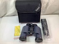 Binocular set with case, cleaning cloth, and strap laid out on table.