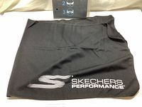 Black Skechers Performance cooling towel folded showing the logo and size relative to a ruler.