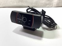 Front view of Thornmax 1080 HD webcam showing camera lens, built-in microphone grills, branding, and USB cable