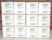 Photo showing 12 white boxes of HP CE410A (HP 305A) black toner cartridges by NuPrint, arranged in a 4x3 grid, each box labeled with part number and key compatibility info.