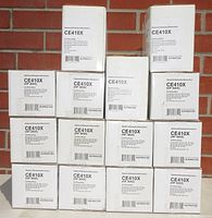 Four rows of boxes labeled CE410X HP 305X containing black toner cartridges by NuPrint, stacked against a brick wall.