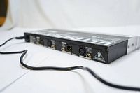 Rear angled view showing input/output connectors including XLR and 1/4 inch TRS inputs and outputs, power cord connected, Behringer logo on rack ears.