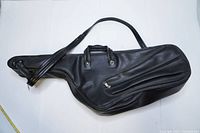 Full view of the black leather saxophone soft case showing shape, handle, strap, and zippered pocket.