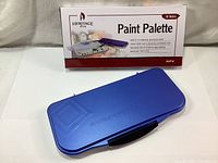 Closed blue plastic paint palette case with box in background