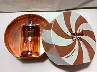 Perfume bottle inside open round gift box with pink and white swirled pattern lid.