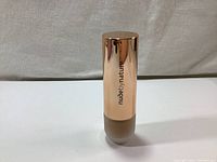 Front view of the frosted glass foundation bottle with rose gold cap, showing brand 'nudebynature' printed on cap.