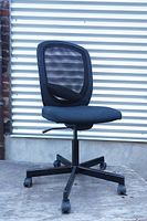 Side view of black office chair with mesh back, padded seat, height adjustment lever, and five caster wheels.