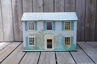 Front view of metallic blue tin toy house with painted door, windows, and foliage details on facade.
