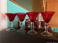 Front view of six cocktail or martini glasses with red bowls and red stems standing in front and clear glasses with frosted peach bands in the back.