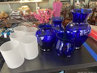 Blue glass vases and white frosted glass sconces displayed together on a black table surface with visible surrounding room items.