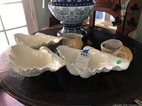Photo showing three white ceramic elongated shell dishes and two tan scallop-shaped shell dishes on a wooden table.