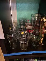 Front view of Coca-Cola glasses and Pat O'Brien hurricane glasses on shelf with variety of sizes and logos.