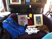 Photo showing blue jacket, Santa hat, Mickey gloves, Chewbacca hat, and two framed Disney prints placed on a purple couch.