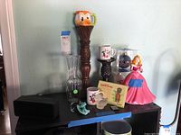 Overview of Disney memorabilia items on black surface including mugs, figurines, candlestick, glass vase, ornaments, and speaker.