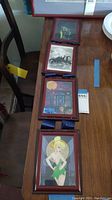 Long view of six framed Disney prints arranged on table showing wooden frames and blue hanging ribbons, various character scenes visible