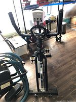 Front view of black stationary exercise bike with handlebars, pedals, and digital display screen.