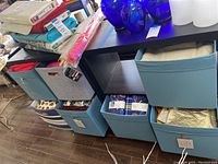 Photo showing the table with stacks of assorted fabric and multiple blue and grey fabric storage cubes underneath filled with fabrics and other items.