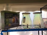 Photo showing two iridescent textured glass beverage dispensers with spigots, unboxed.