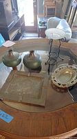 Overview of all metal home decor items on a wooden table with glass top showing the ashtray, candle holders, and decorative bowl