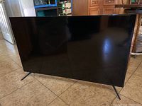 Front view of the 50-inch black Insignia LED TV with the screen facing forward, standing on two angled legs on tile floor.