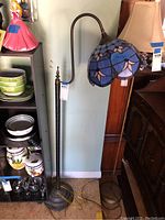 Full view of stained glass floor lamp showing stand, curved arm, and blue-pink floral shade.