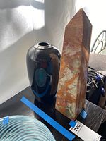 Photo showing side view of the stone obelisk and black vase on a surface with light reflecting on them.