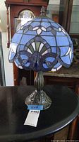 Full view of stained glass Tiffany style lamp with blue floral motif and metal base.
