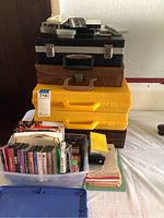 Stacked collection including several black and yellow tape storage cases with a bin of cassette tapes and books beside them