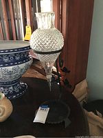 Full view of the vintage glass wine decanter with diamond-pattern texture, shown held in black metal stand on wooden table.