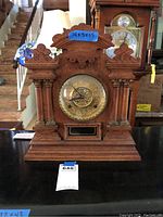 Full front view of vintage wooden mantel clock on display with visible carved woodwork and brass clock face.